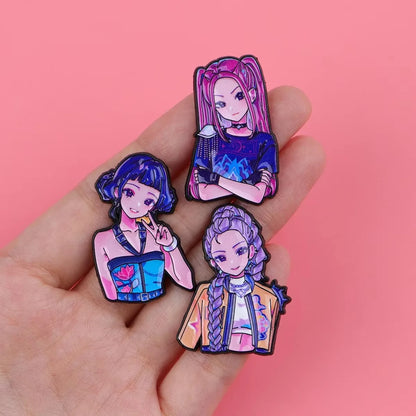 Three colorful anime-style enamel pins held on a person's fingers against a solid pink background.