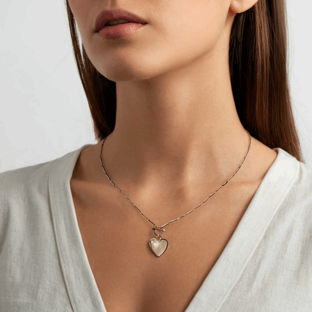 Necklace with a heart-shaped pendant worn by a person on a plain background
