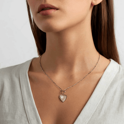 Necklace with a heart-shaped pendant worn by a person on a plain background
