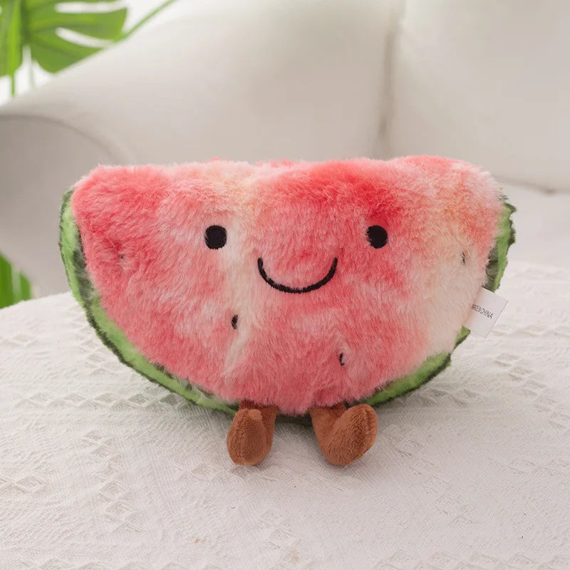 A plush watermelon slice cushion with embroidered facial features and small brown legs, resting on a white textured surface with a soft white background.