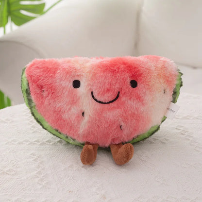 A plush watermelon slice cushion with embroidered facial features and small brown legs, resting on a white textured surface with a soft white background.