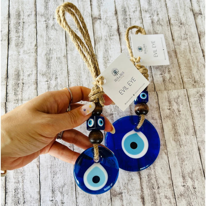Hand holding blue evil eye keychains with a wooden background
