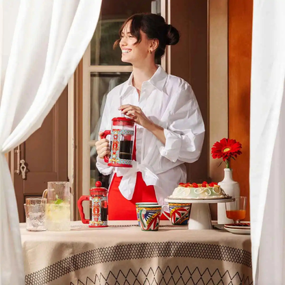 Woman in a white shirt holding a red and white pitcher with a table of drinks and a cake in the background.