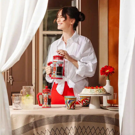 Woman in a white shirt holding a red and white pitcher with a table of drinks and a cake in the background.
