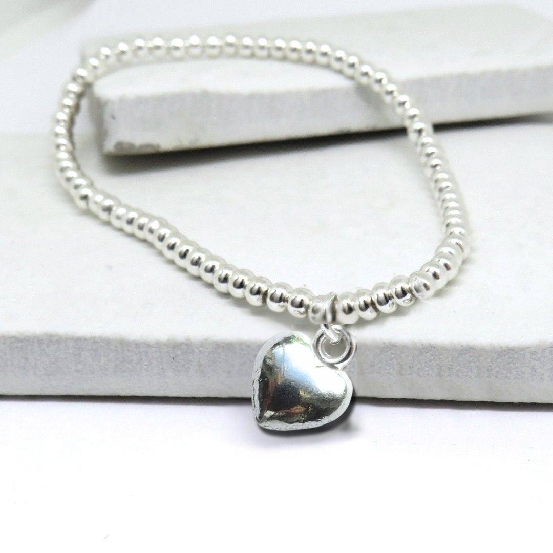 Silver beaded bracelet with a heart charm on a white background