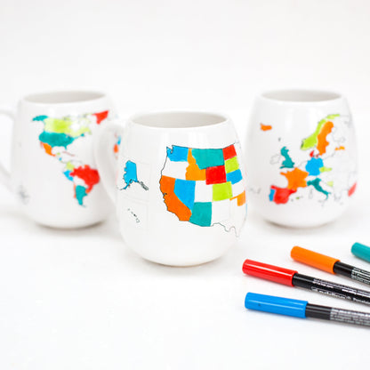 Three white ceramic cups with colorful map designs on a white background, accompanied by markers.