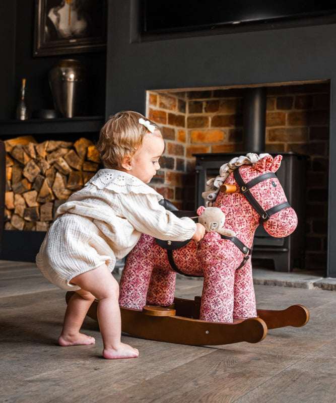 Child playing with a rocking horse in a cozy living room with a fireplace.