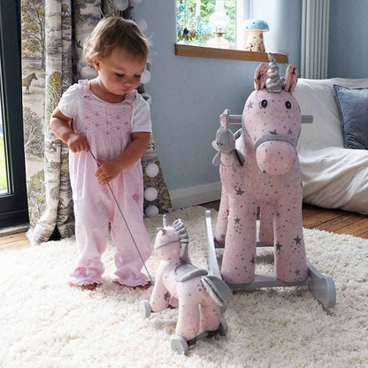 Child playing with a pink rocking horse toy in a room with a window and furniture.