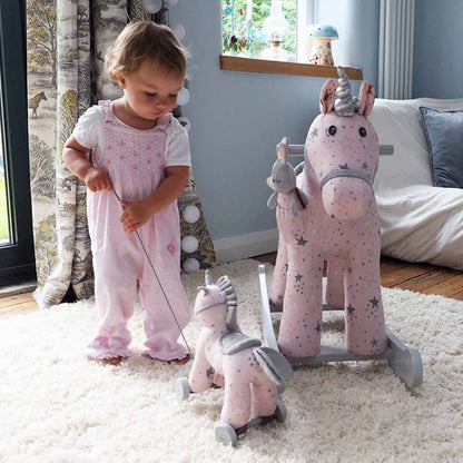 Child playing with a pink rocking horse toy in a room with a window and furniture.