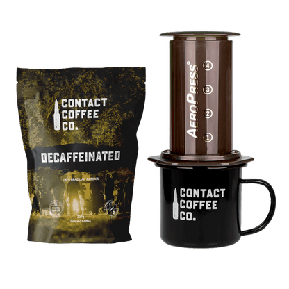 Decaffeinated coffee package, AeroPress coffee maker, and Contact Coffee Co. mug on a white background