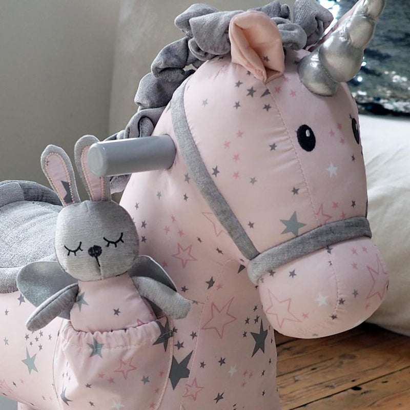 Pink unicorn plush toy with star pattern and gray rabbit plush toy on a wooden floor.