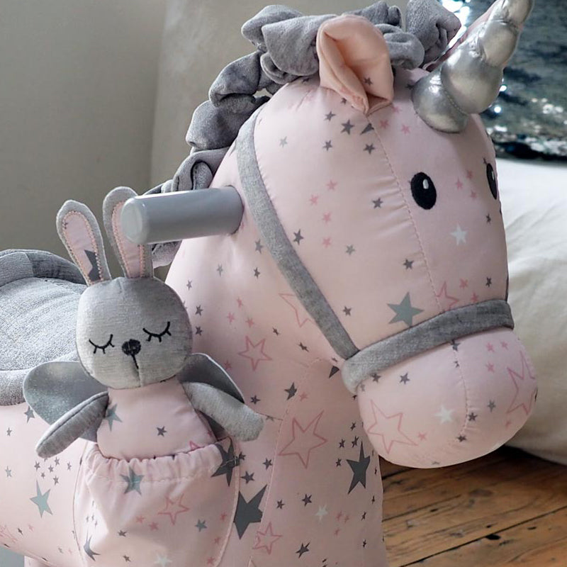 Pink unicorn plush toy with star pattern and gray rabbit plush toy on a wooden floor.