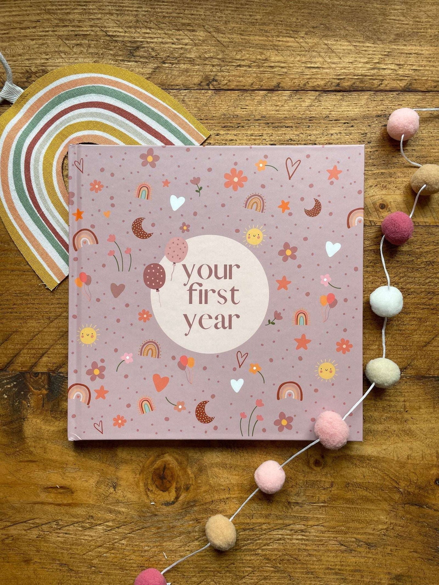 Pink book titled 'your first year' on a wooden surface with decorative elements.