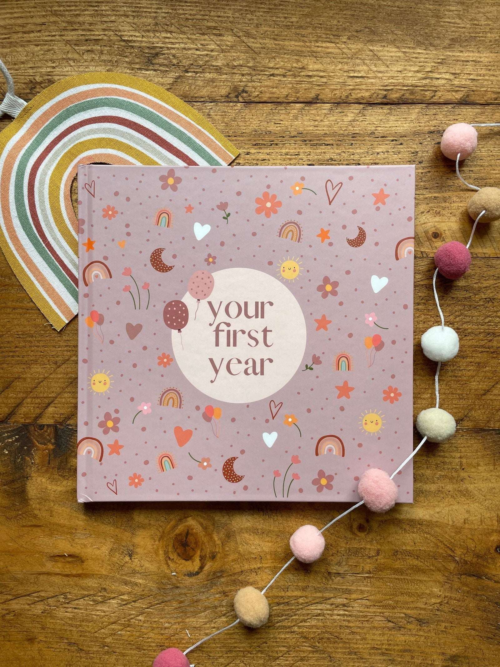 Pink book titled 'your first year' on a wooden surface with decorative elements.