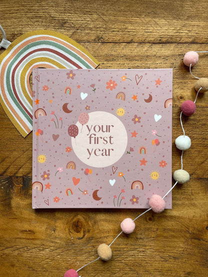 Pink book titled 'your first year' on a wooden surface with decorative elements.