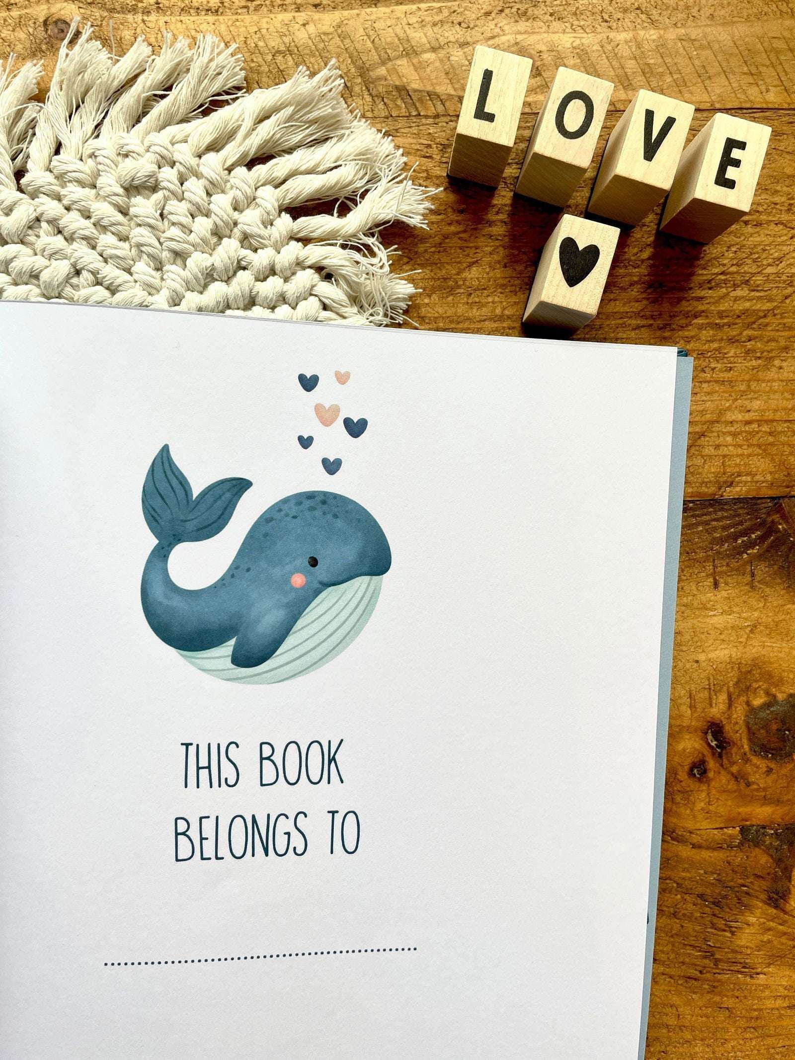 Book with a whale illustration and 'This book belongs to' text on a wooden surface with decorative elements.