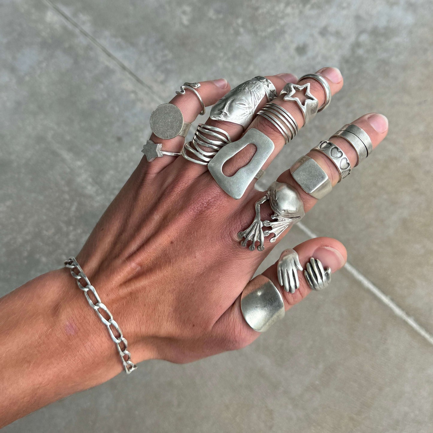 Hand wearing multiple silver rings on a neutral background