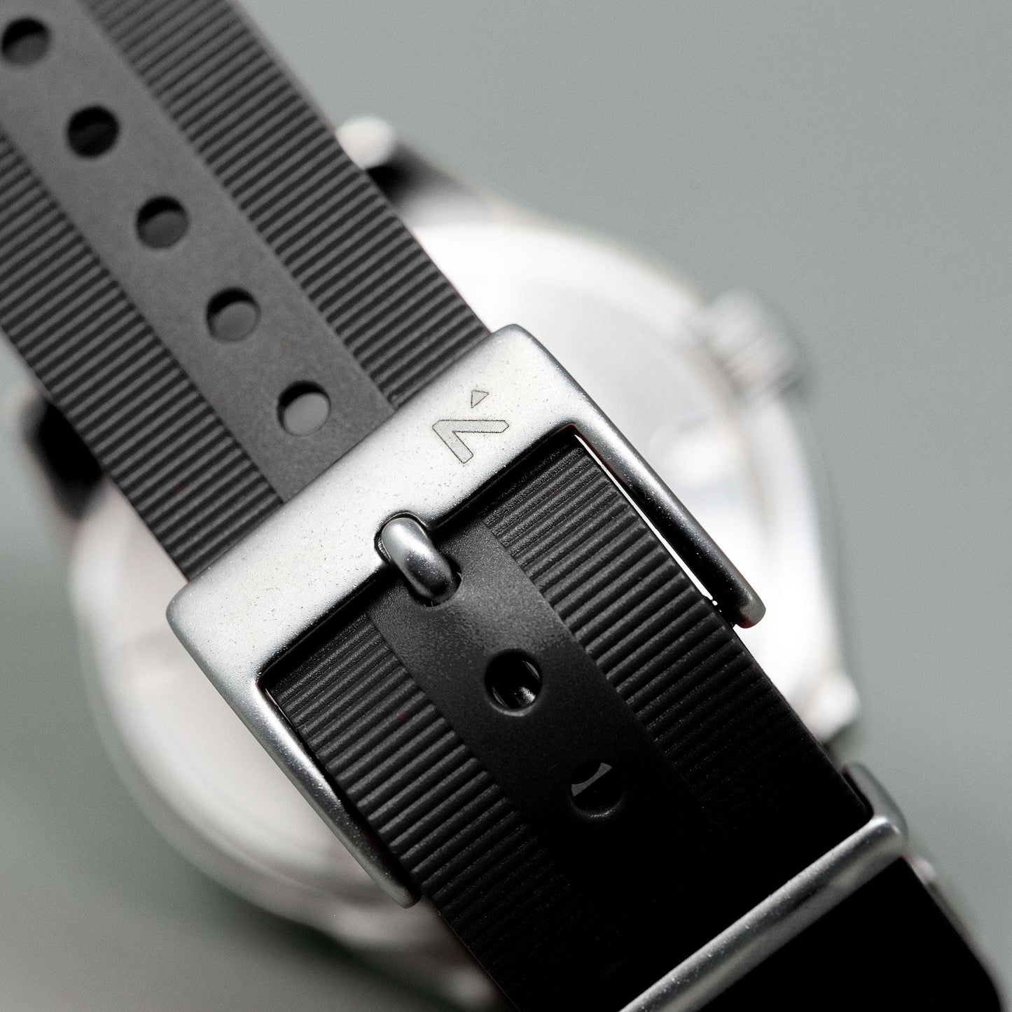 Close-up of a watch with a black strap and silver buckle on a gray background
