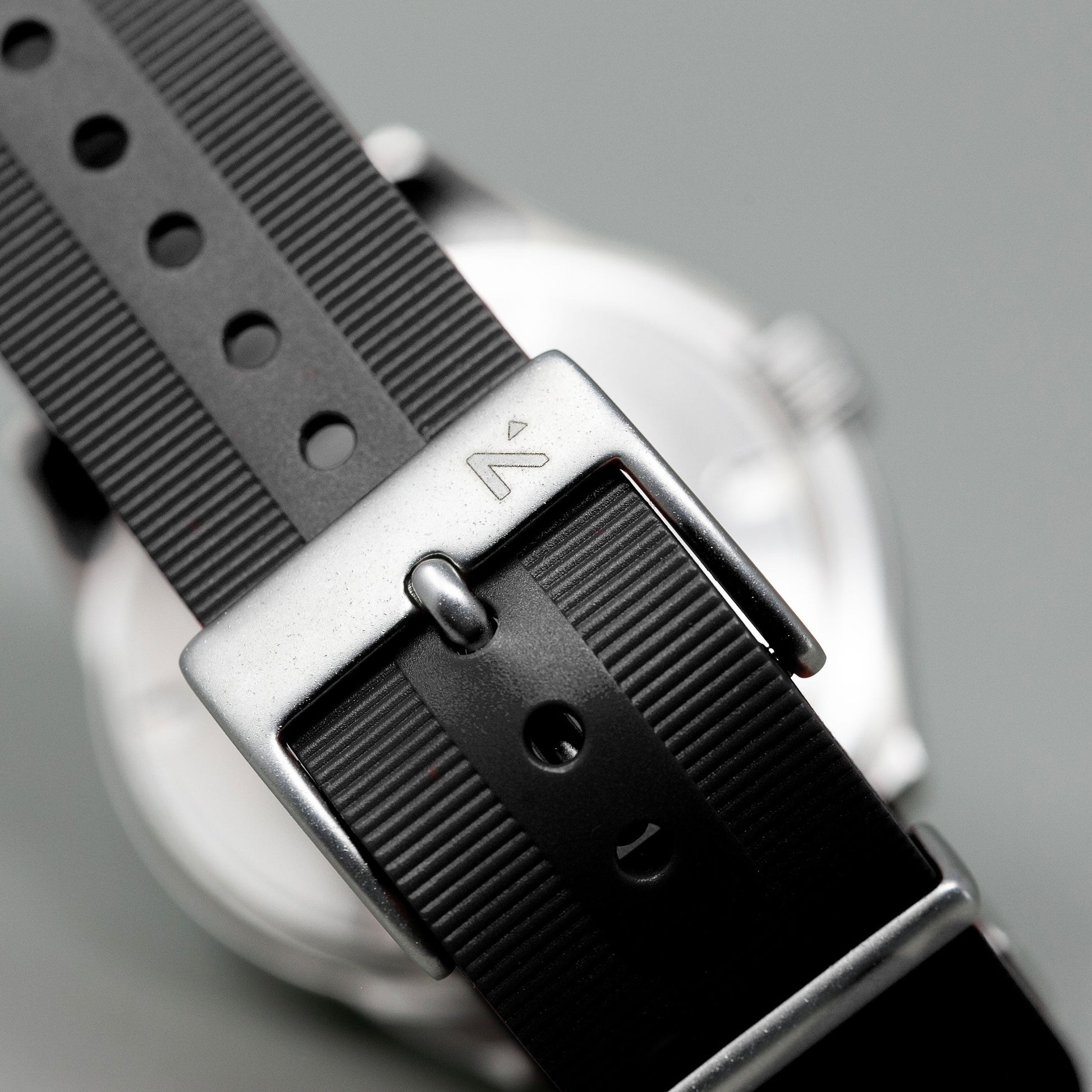 Close-up of a watch with a black strap and silver buckle on a gray background