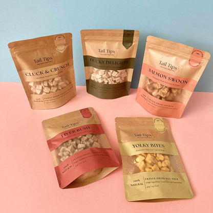 Five packages of Tail Tips pet treats on a pink and blue background