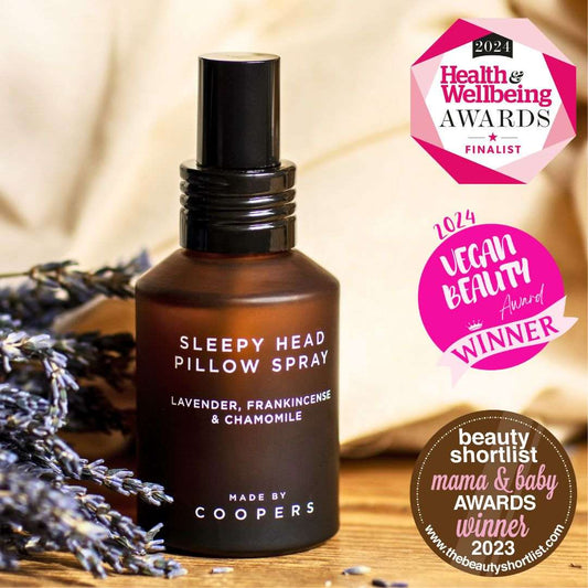 Sleepy Head Pillow Spray bottle with lavender, on a wooden surface, surrounded by lavender flowers, with awards logos displayed.