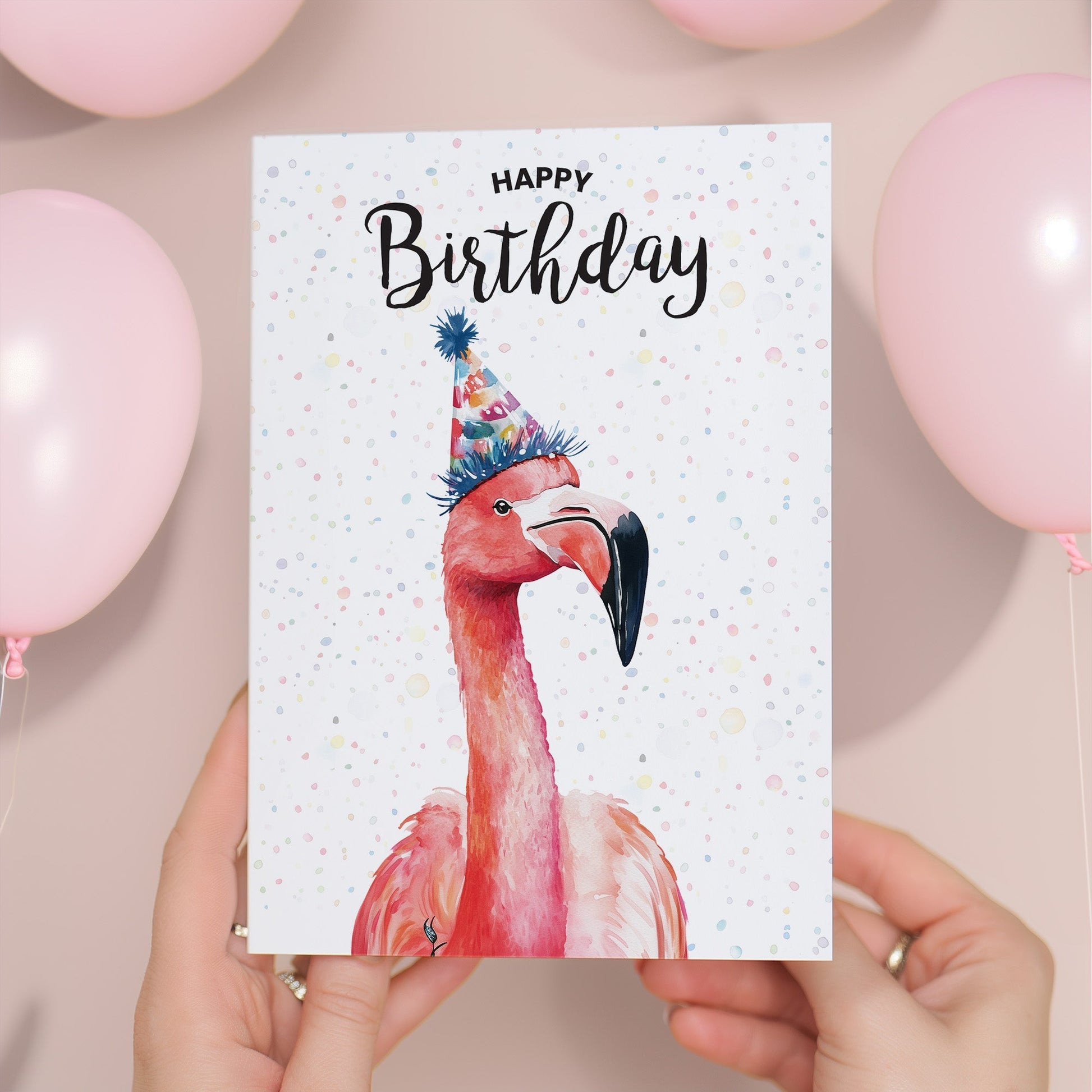 Birthday card with a flamingo wearing a party hat held by hands with balloons in the background