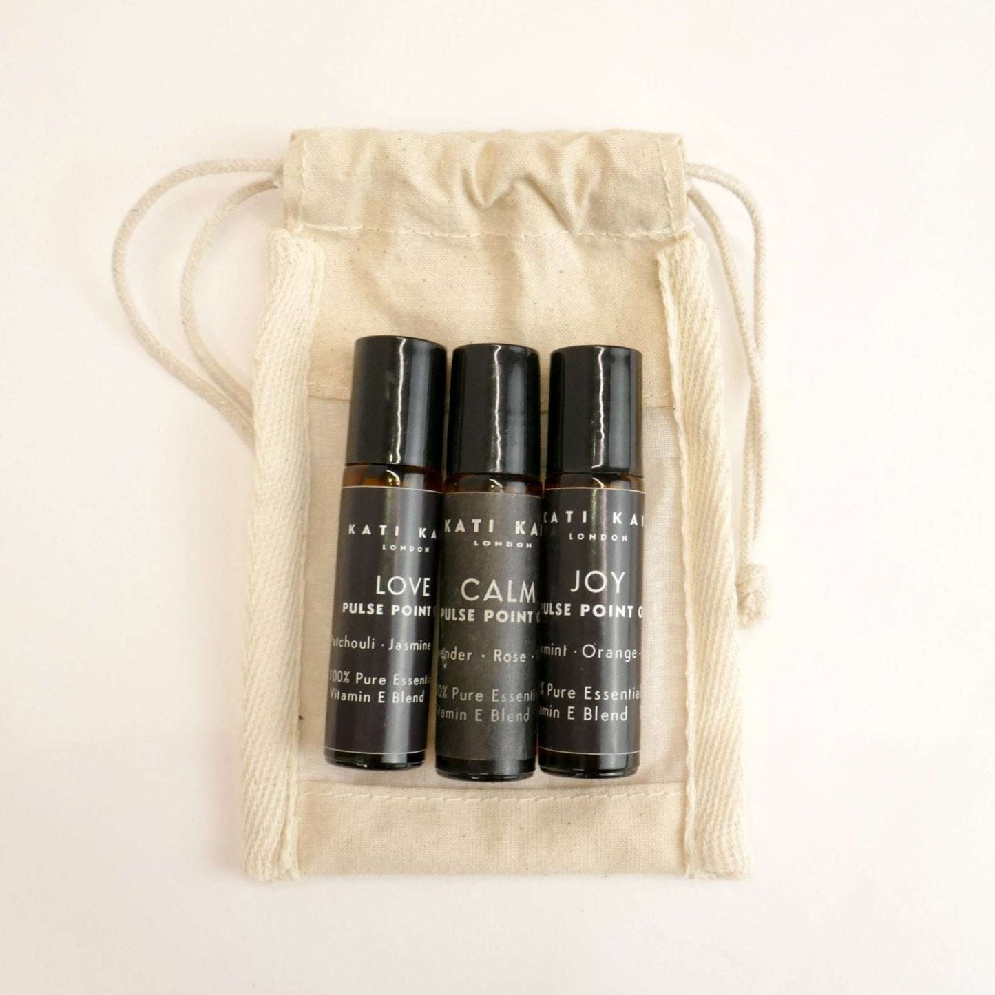 Three black rollerball bottles labeled 'Love', 'Calm', and 'Joy' in a beige drawstring bag.
