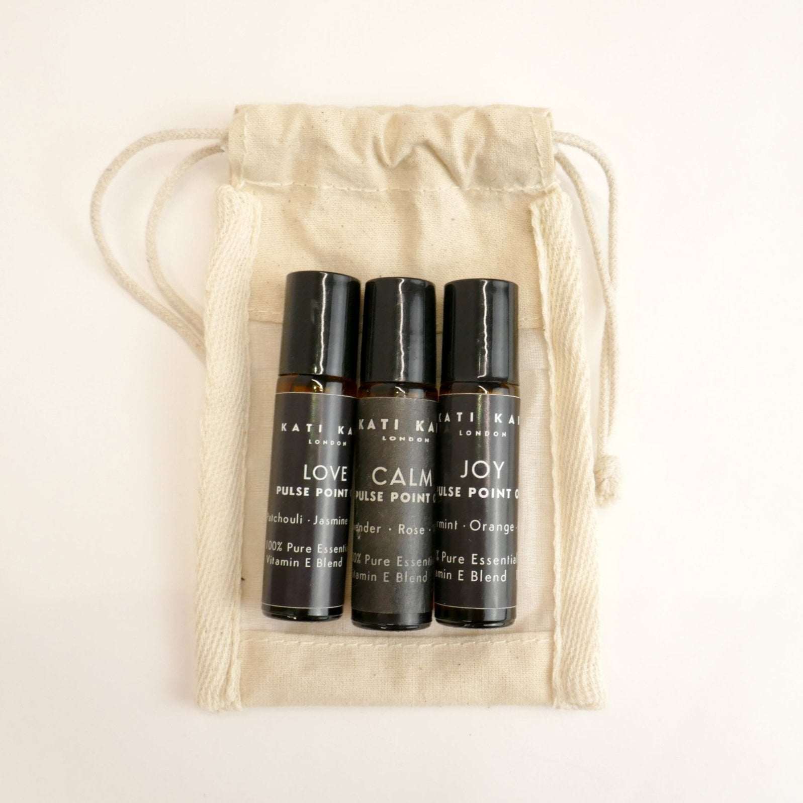 Three black rollerball bottles labeled 'Love', 'Calm', and 'Joy' in a beige drawstring bag.