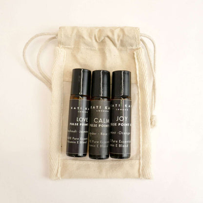 Three black rollerball bottles labeled 'Love', 'Calm', and 'Joy' in a beige drawstring bag.