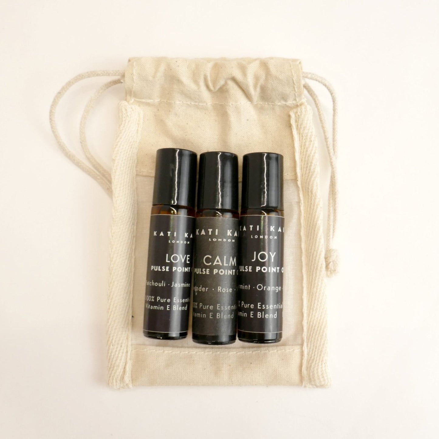 Three black rollerball bottles labeled 'Love', 'Calm', and 'Joy' in a beige drawstring bag.