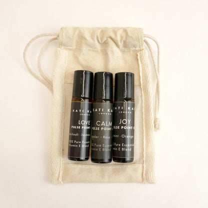 Three black rollerball bottles labeled 'Love', 'Calm', and 'Joy' in a beige drawstring bag.