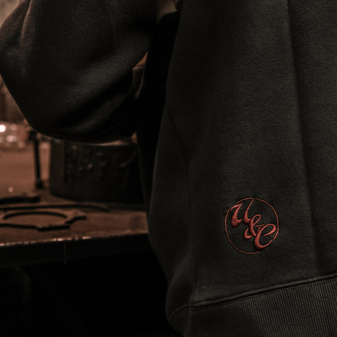 Dark hoodie with a logo on the sleeve against a blurred background