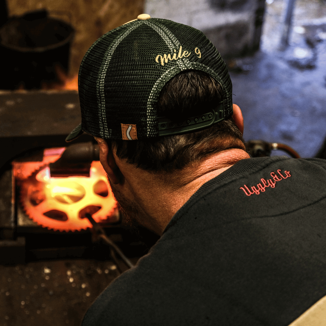 Person wearing a black cap and black shirt with red text, working on a glowing metal object.