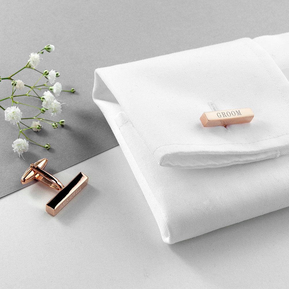Rose gold cufflinks and tie slide on a white fabric background with flowers.