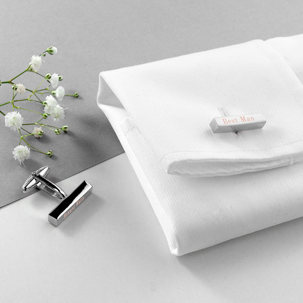 Cufflinks and a tie clip on a white shirt with flowers on a gray surface