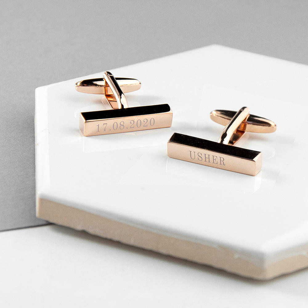 Rose gold cufflinks with engraved text on a white surface