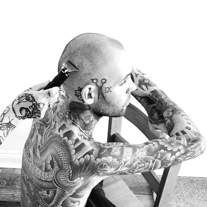 Man with extensive tattoos sitting on a chair.