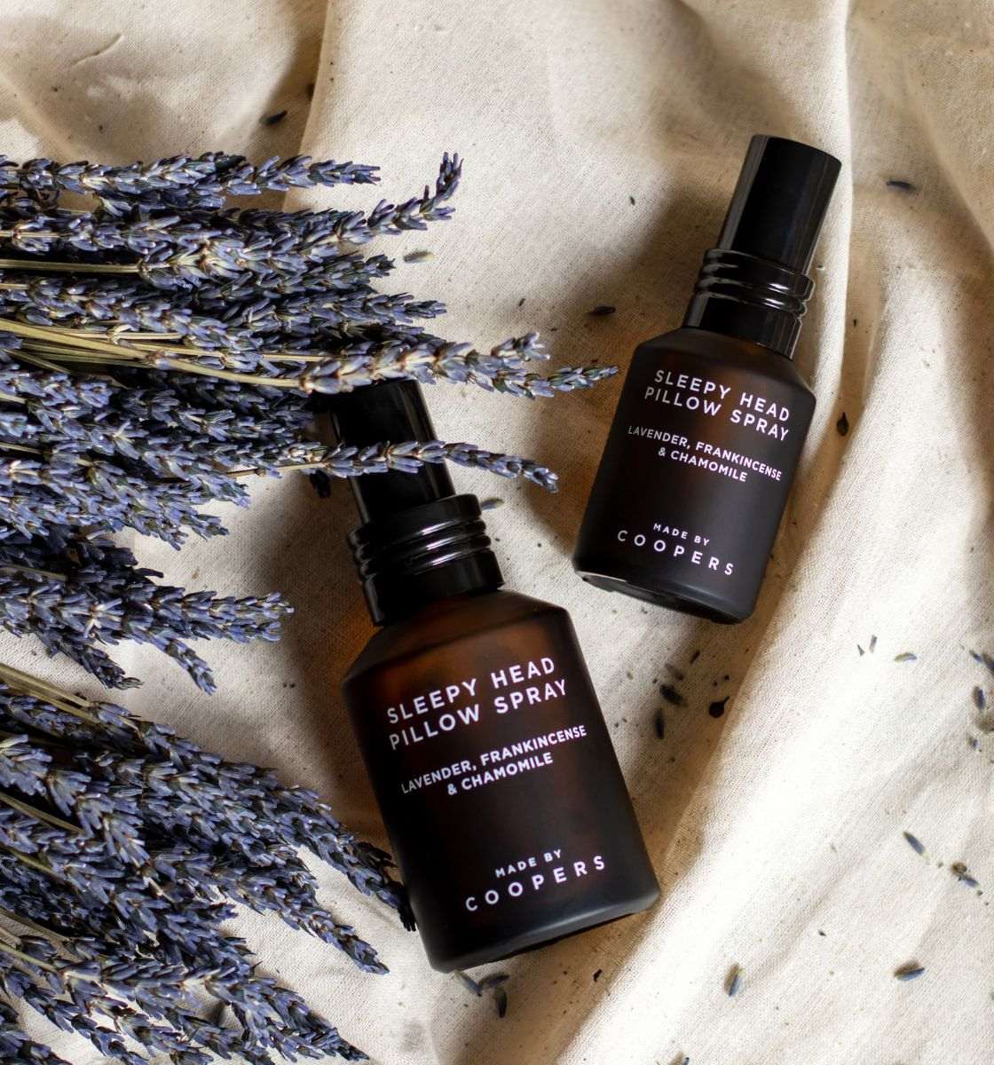 Two bottles of 'Sleepy Head Pillow Spray' by Made by Coopers on a textured fabric background with lavender.