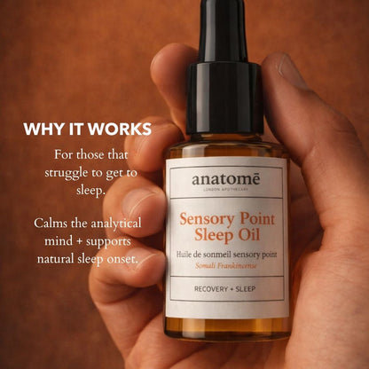 Hand holding a bottle of 'Sensory Point Sleep Oil' by anatomè with text explaining its benefits on a brown background.