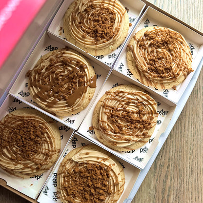 Six round cookies with a swirled topping in a box on a wooden surface