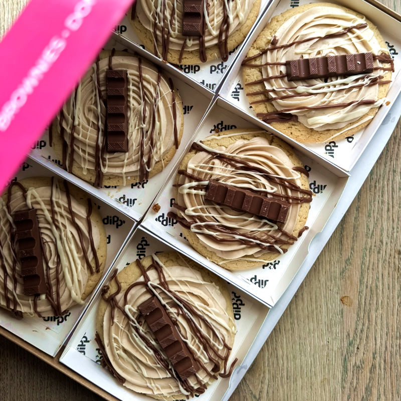 Box of cookies with chocolate drizzle and Kinder bars on a wooden surface