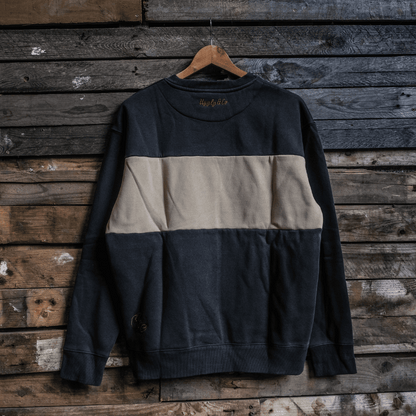 Two-tone black and beige sweatshirt hanging on a wooden hanger against a rustic wooden wall.