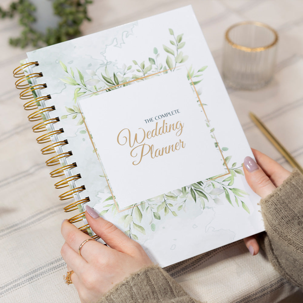 Wedding planner book with greenery design held by a person on a neutral background