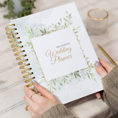 Wedding planner book with greenery design held by a person on a neutral background