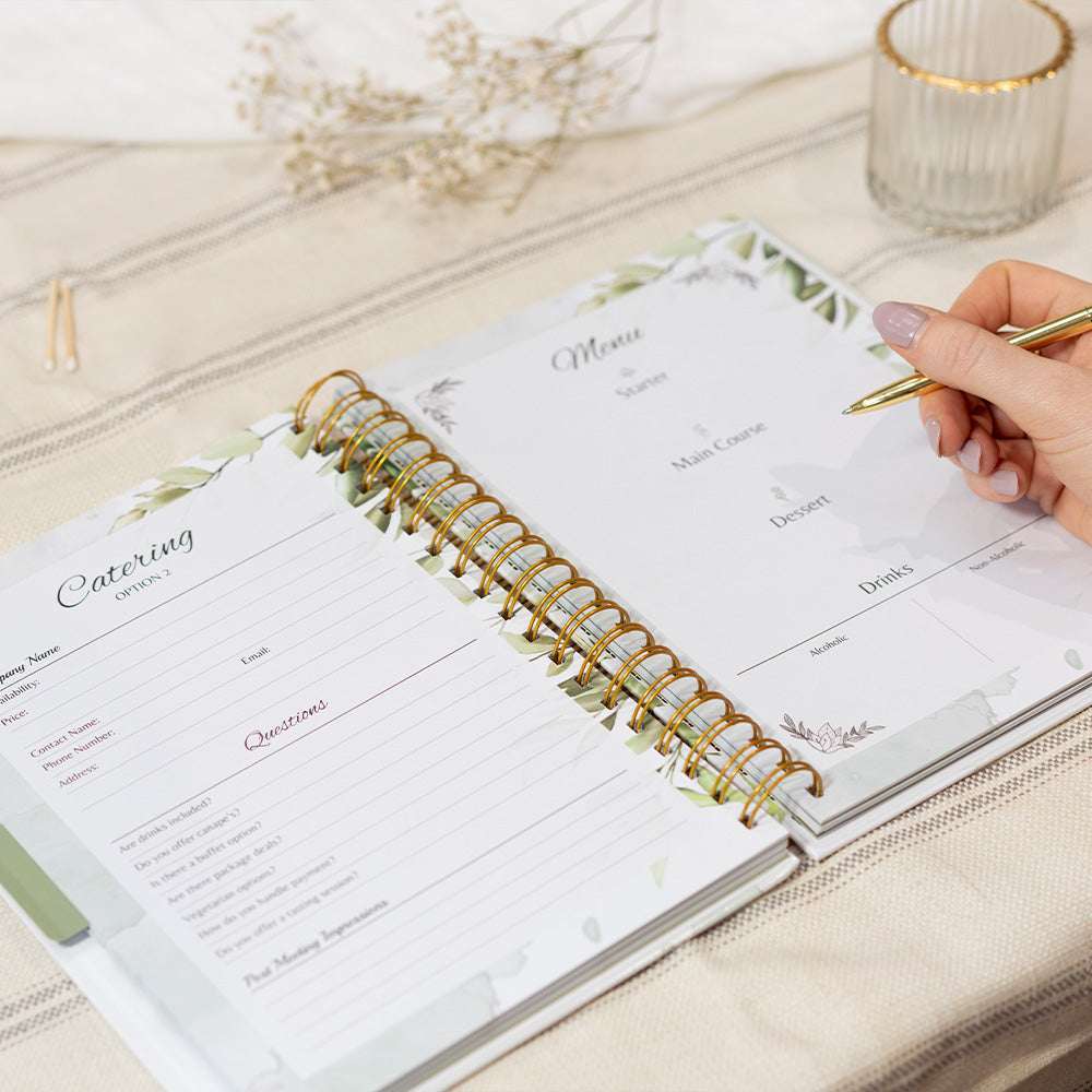 Open planner with spiral binding on a light surface, hand holding a pen.