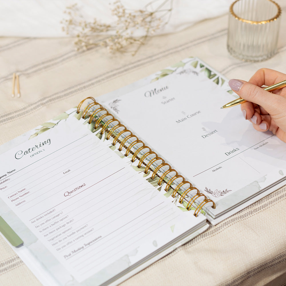 Open planner with spiral binding on a light surface, hand holding a pen.